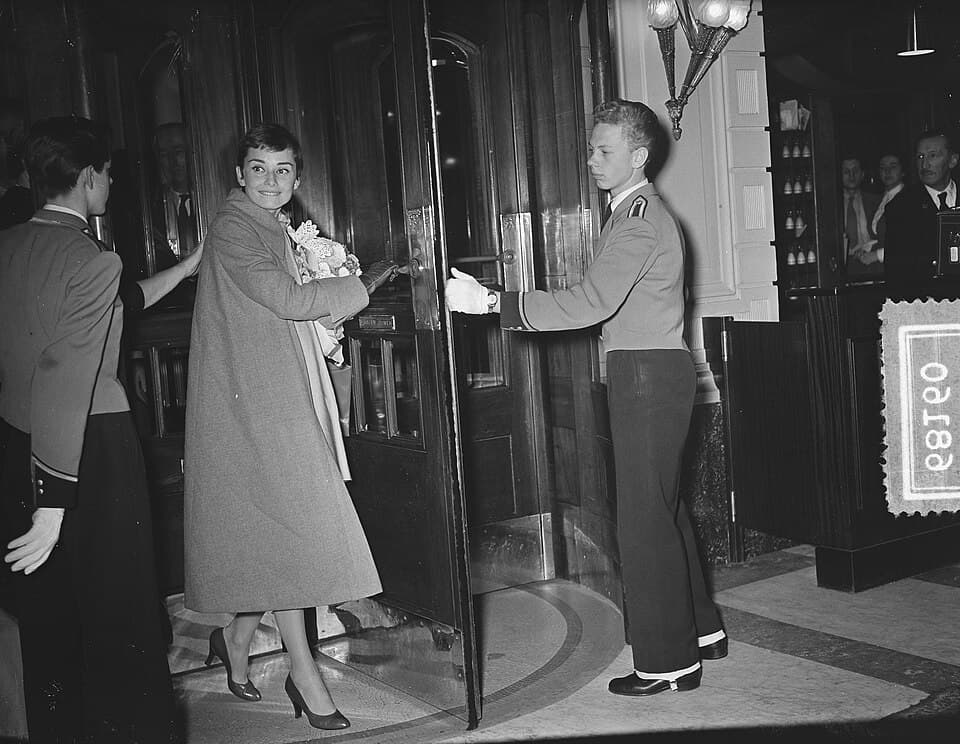 Audrey Hepburn arriving at a building in Amsterdam in 1954, turning towards the camera