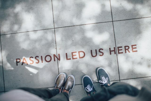 Two people standing on a paved surface with the words Passion Led Us Here written between them