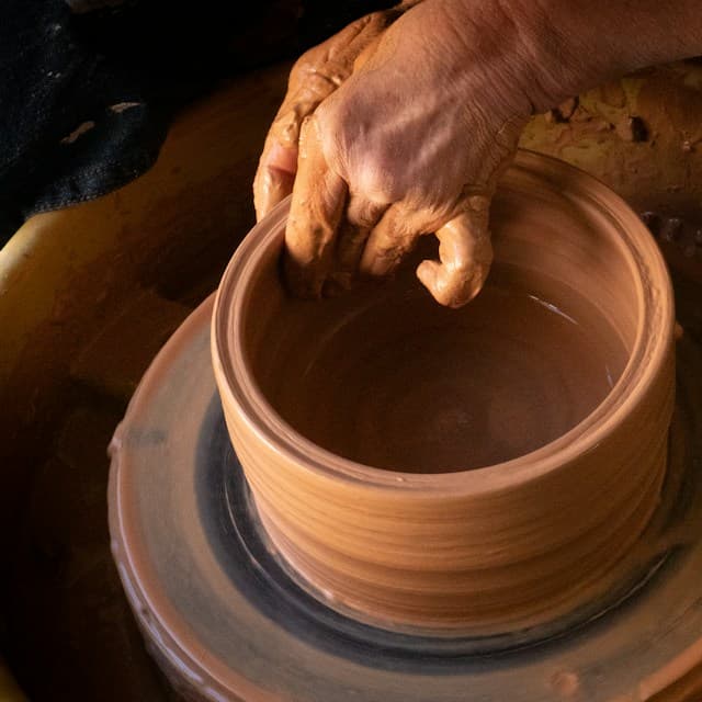 A potter's hands shaping a clay vessel on a spinning pottery wheel.