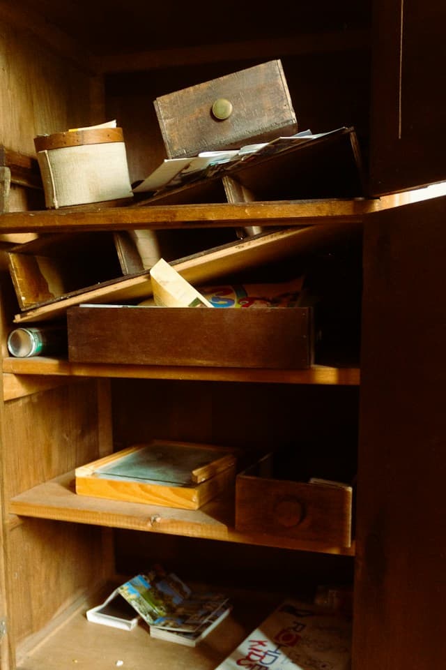 Old wooden shelving filled with drawers, boxes and scattered papers, photographed in a disused interior.