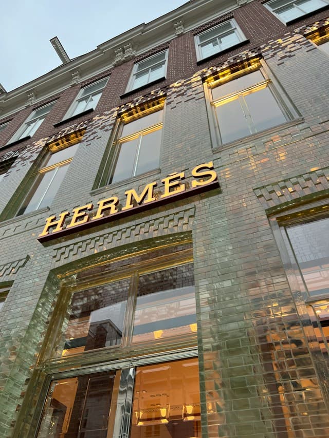The illuminated Hermès sign above the entrance of a brick and tiled boutique building in Amsterdam.
