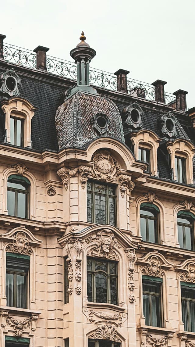 An ornate historic European building with decorative stone carvings, elegant windows and a dark mansard roof